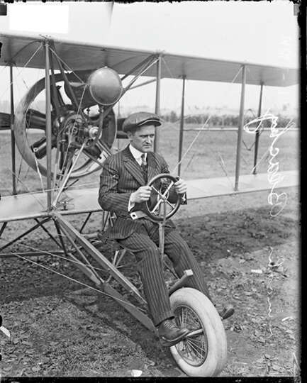 Lincoln Beachey sits in an airplane on a dirt field.