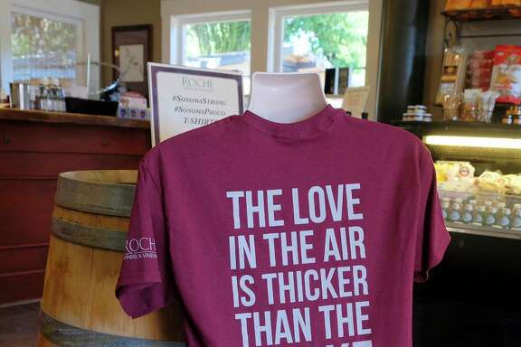 In this photo taken Saturday, Oct. 28, 2017, a t-shirt referencing the recent wildfires is shown for sale in the tasting room at Roche Winery and Vineyards in Sonoma, Calif. The impact the wildfires had on the wine industry was minimal overall, but many face challenges making up for losses sustained during closures at the busiest time of year and now convincing people to revisit. (AP Photo/Eric Risberg)