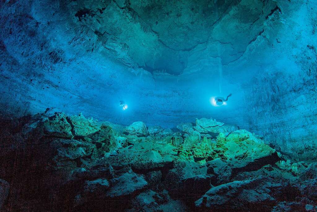 In this undated photo made available by Roberto Chavez Arce in May 2014, divers use lights to illuminate Hoyo Negro, an underwater cave in Mexico's Yucatan Peninsula where the remains of "Naia," a teenage girl who lived 12,000 to 13,000 years earlier, were found. Her skeleton and her DNA are helping scientists study the origins of the first Americans. An analysis of her remains was released Thursday, May 15, 2014 by the journal Science. Her DNA links her to an ancient land bridge connecting Asia and North America, and suggests she shares ancestors with the modern native peoples of the Americas. (AP Photo/Roberto Chavez Arce via Science) Photo: Roberto Chavez Arce, Associated Press